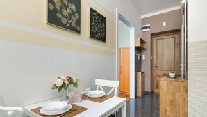 A dining area with a white table set for two, a vase with flowers, and two framed botanical prints on the wall.