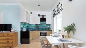 Una cocina moderna con salpicadero azul, armarios blancos y un área de comedor con una mesa y sillas blancas.