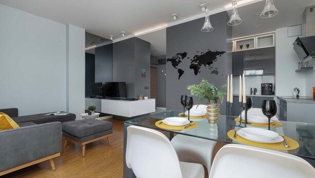 A modern living room with a glass dining table, white chairs, and a grey sofa.