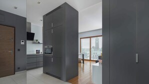 A modern kitchen with grey cabinets, a wooden floor, and a city view through large windows.