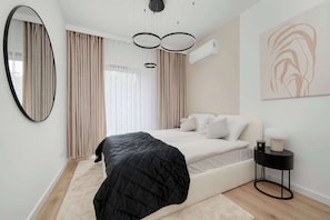 Een moderne slaapkamer met een bed, een ronde spiegel, een nachtkastje en een wandairconditioner.