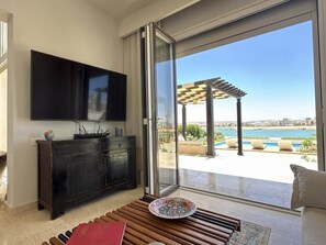 Un salon moderne doté d’un grand téléviseur, d’une table basse en bois et offrant une vue sur une piscine et un espace extérieur.