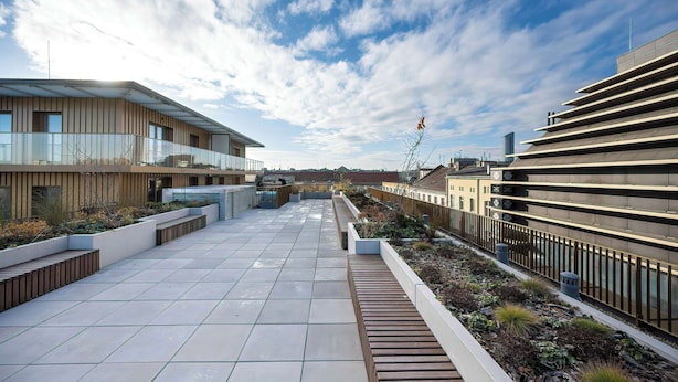 Une terrasse moderne située sur le toit, avec un sol carrelé, des jardinières en bois et une vue sur les bâtiments environnants.