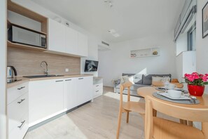 Una cocina moderna con armarios blancos, un microondas y una encimera de madera. Hay una zona de comedor con una mesa, sillas y un jarrón con flores rojas.