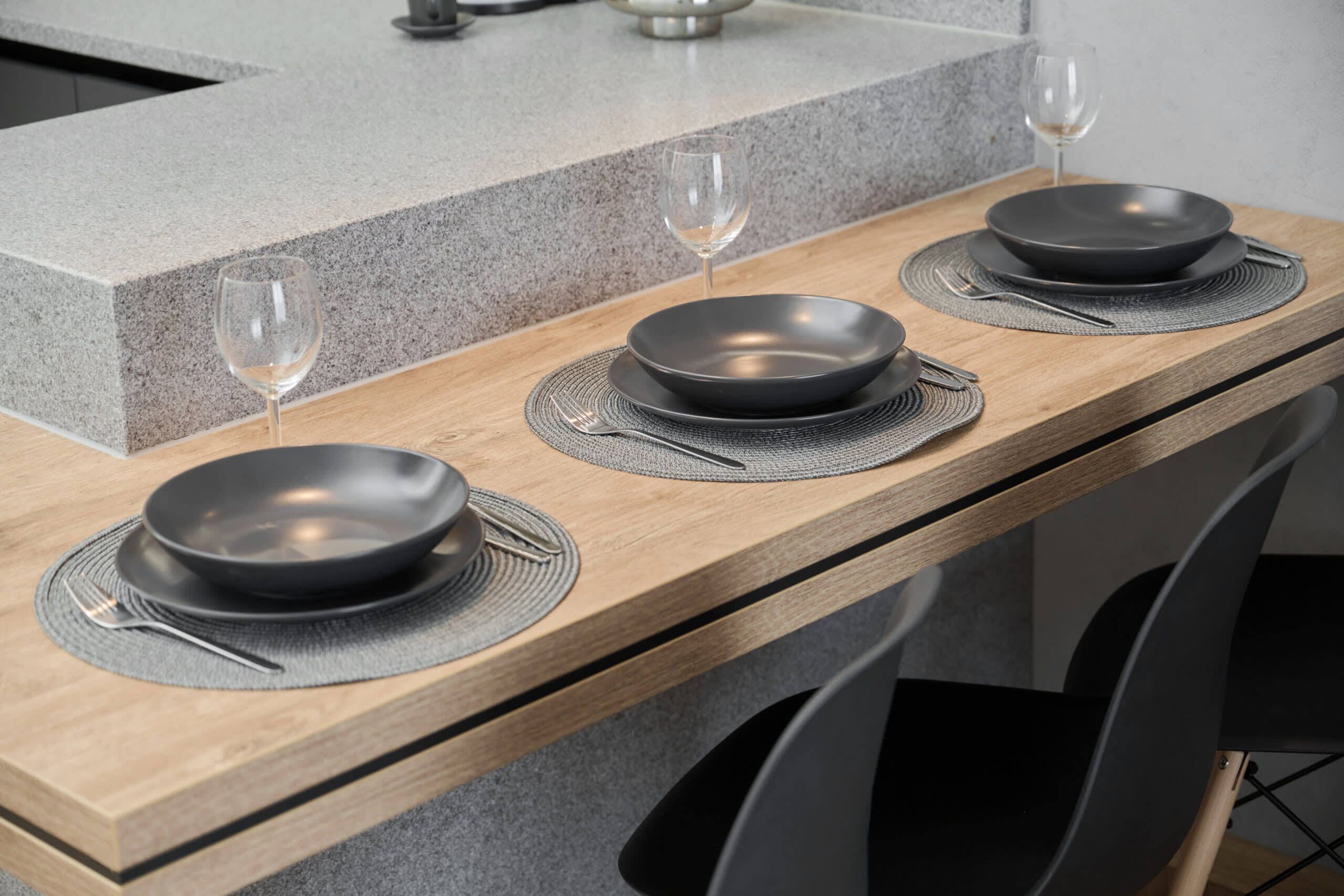 A kitchen counter with three black plates, two wine glasses, and a wooden table.