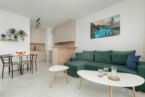 Uma sala de estar moderna com um sofá verde, uma mesa de jantar com cadeiras e uma área de cozinha ao fundo.