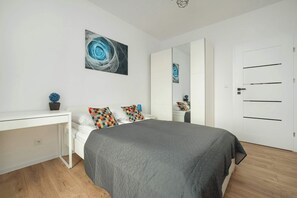 Quarto com cama, escrivaninha branca, espelho e porta.