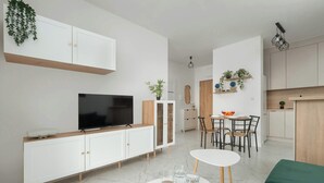 Un espacio habitable moderno con televisor, armarios blancos, comedor y cocina.