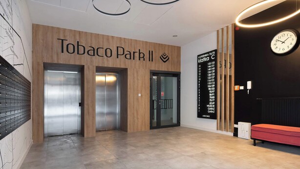 Un hall con pared de madera, dos ascensores, un banco rojo y un reloj.