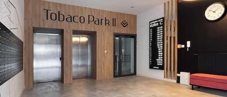 Un hall con pared de madera, dos ascensores, un banco rojo y un reloj.