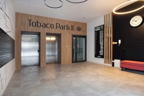 Un hall con pared de madera, dos ascensores, un banco rojo y un reloj.