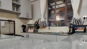Eine Küche mit Gasherd, Spüle und Schränken. Ein Fenster mit Vorhängen bietet Blick ins Freie.