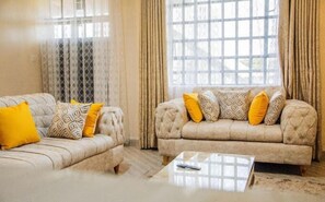 Una sala de estar con dos sofás, una mesa de centro y un ventanal con cortinas.