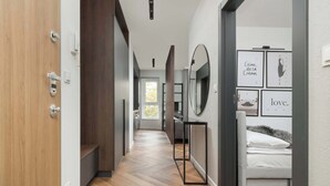A modern hotel hallway with a wooden floor, a bed with white bedding, and framed artwork on the wall.