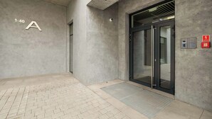 A modern building entrance with a concrete facade, a glass door, and a fire alarm box.
