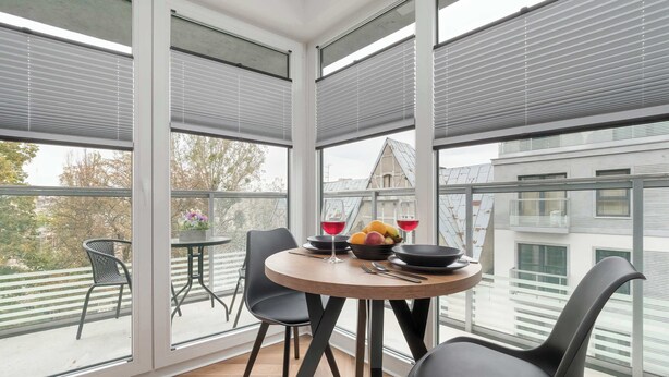 A balcony with a round table, chairs, and a bowl of fruit and wine glasses.