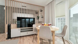 Una cocina moderna con separador de madera, televisor integrado y zona de comedor con mesa redonda y sillas.
