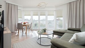 Una sala de estar moderna con un sofá, una mesa de comedor con sillas y un ventanal con persianas.