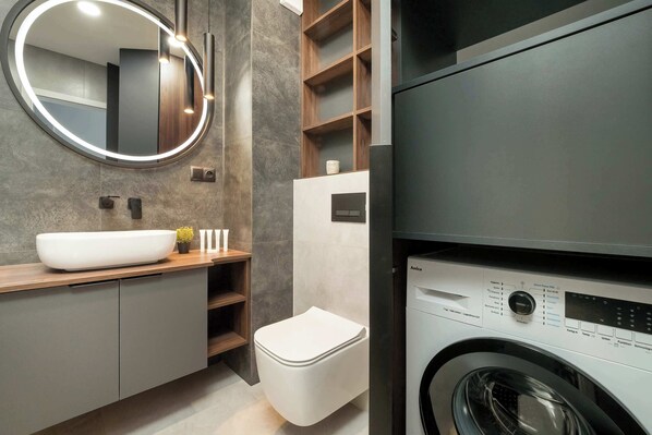 Un baño moderno con un espejo grande, lavabo, inodoro y lavadora integrada.