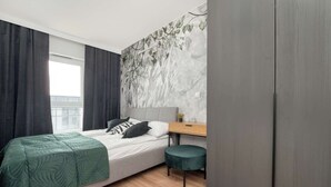 Un dormitorio moderno con cama, escritorio pequeño, reposapiés verde y armario.