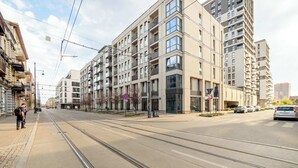 Una calle urbana moderna con vías de tranvía, edificios residenciales de varios pisos y coches aparcados.
