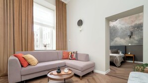 Ein modernes Wohnzimmer mit einer Eckcouch, einem runden Couchtisch und einem großen Fenster mit Vorhängen.
