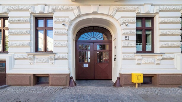 Ein Gebäudeeingang mit doppeltürigem Eingang, einer Nummertafel und einem gelben Schild.