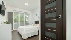 A bedroom with a bed, a dresser, a TV, and a door with frosted glass panels.