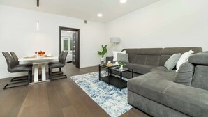 A modern living room with a grey sofa, a dining table with chairs, and a coffee table.