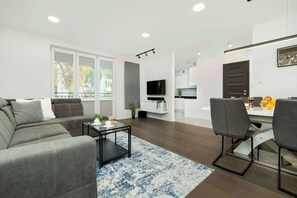 A modern living room with a gray sofa, a coffee table, and a dining area with chairs and a table.