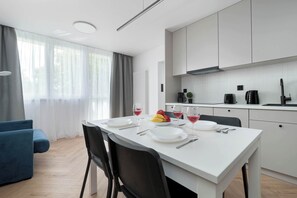 Una cocina moderna con armarios blancos, una mesa de comedor dispuesta con platos, vasos y cubiertos, y un sofá azul en la sala de estar contigua.