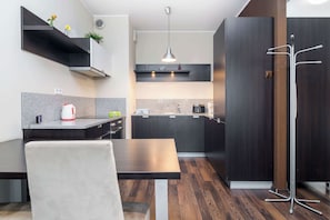 A modern kitchen with dark wood cabinets, a granite countertop, and a dining area with a wooden table and a white chair.