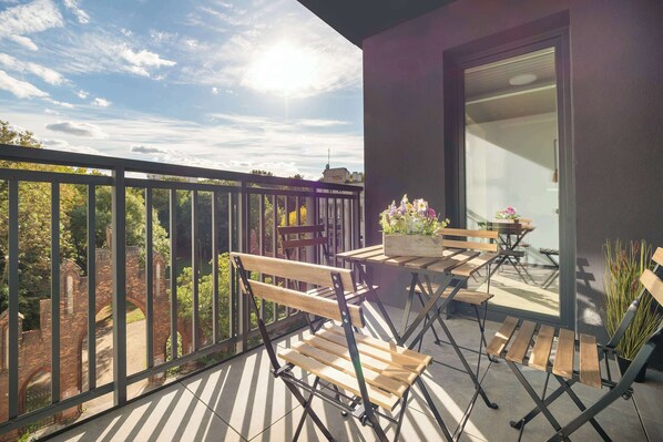 Un balcón con vista a un arco de ladrillo, sillas de madera, una mesa y una planta en maceta.