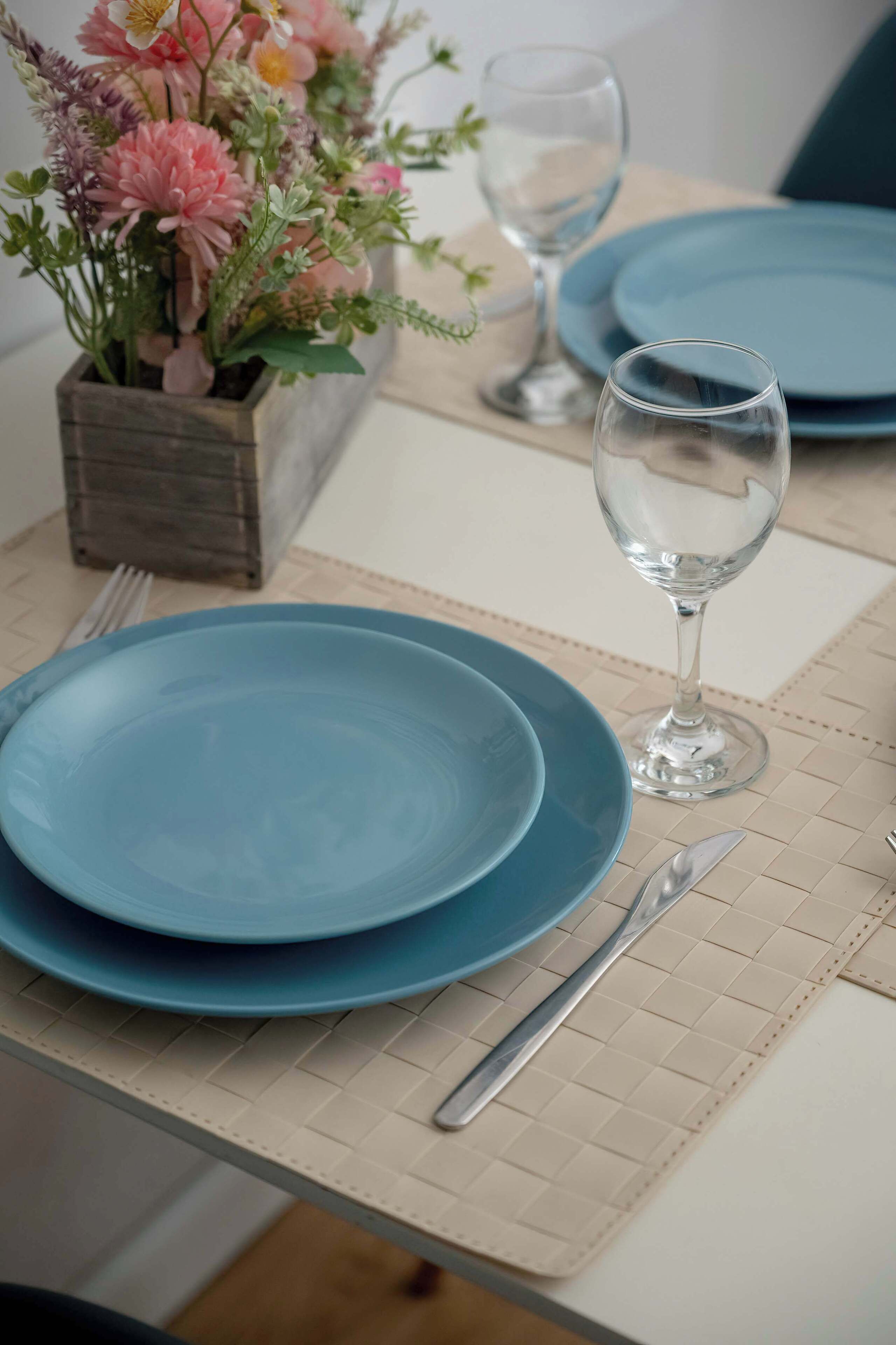 A table set with blue plates, a wine glass, and a floral centerpiece.