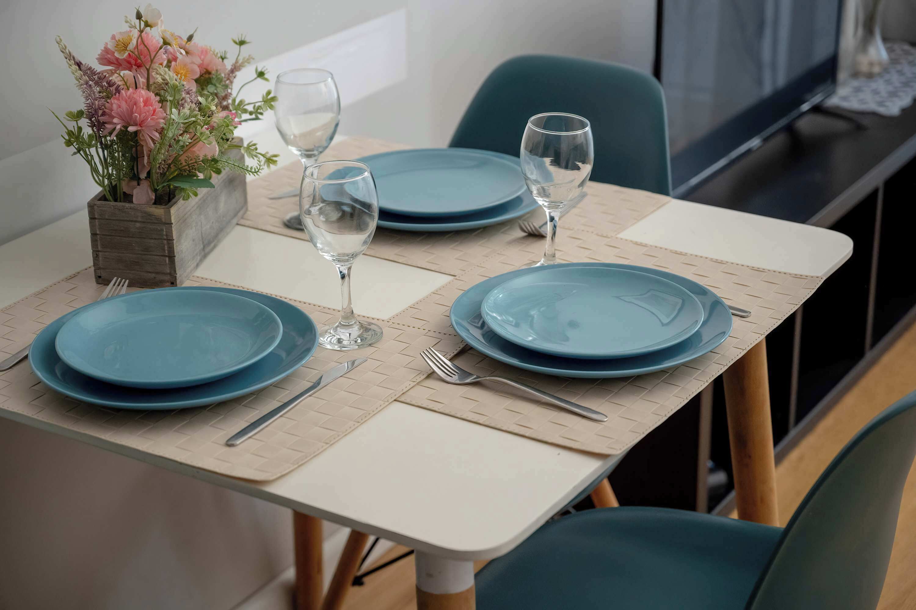 A dining table set with blue plates, wine glasses, and a small potted plant.