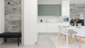 Eine moderne Küche mit weißen Schränken, einer Marmor-Spritzschutzwand und einem Essbereich mit weißem Tisch und Stühlen.