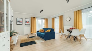 Una sala de estar moderna con un sofá azul, una mesa de comedor con sillas y un amplio ventanal con cortinas.