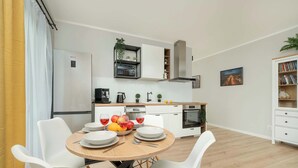 Una cocina moderna con armarios blancos, horno empotrado y comedor con una mesa redonda y sillas blancas.