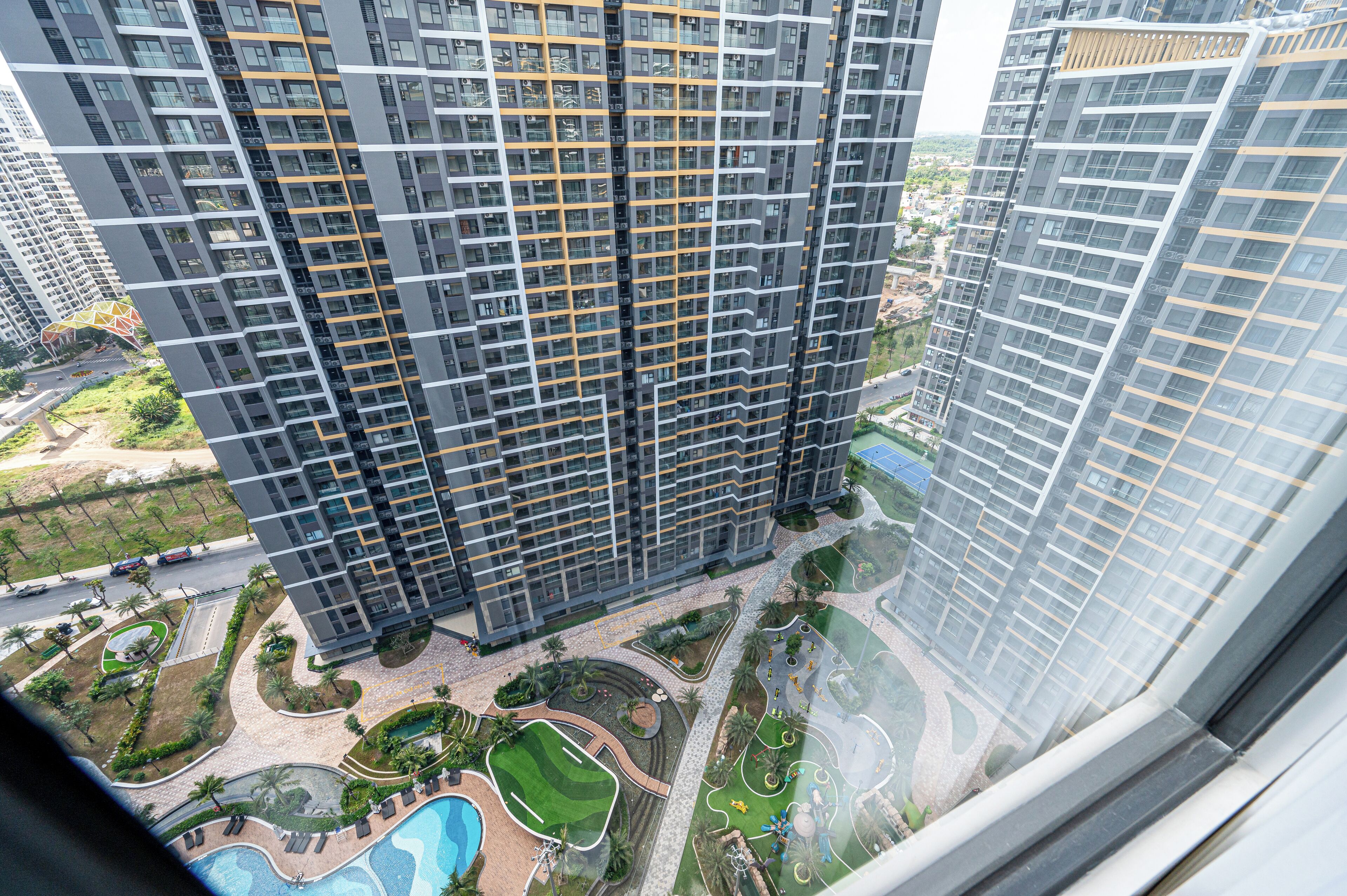 Un edificio residencial alto con múltiples balcones, un patio ajardinado con senderos y una piscina.
