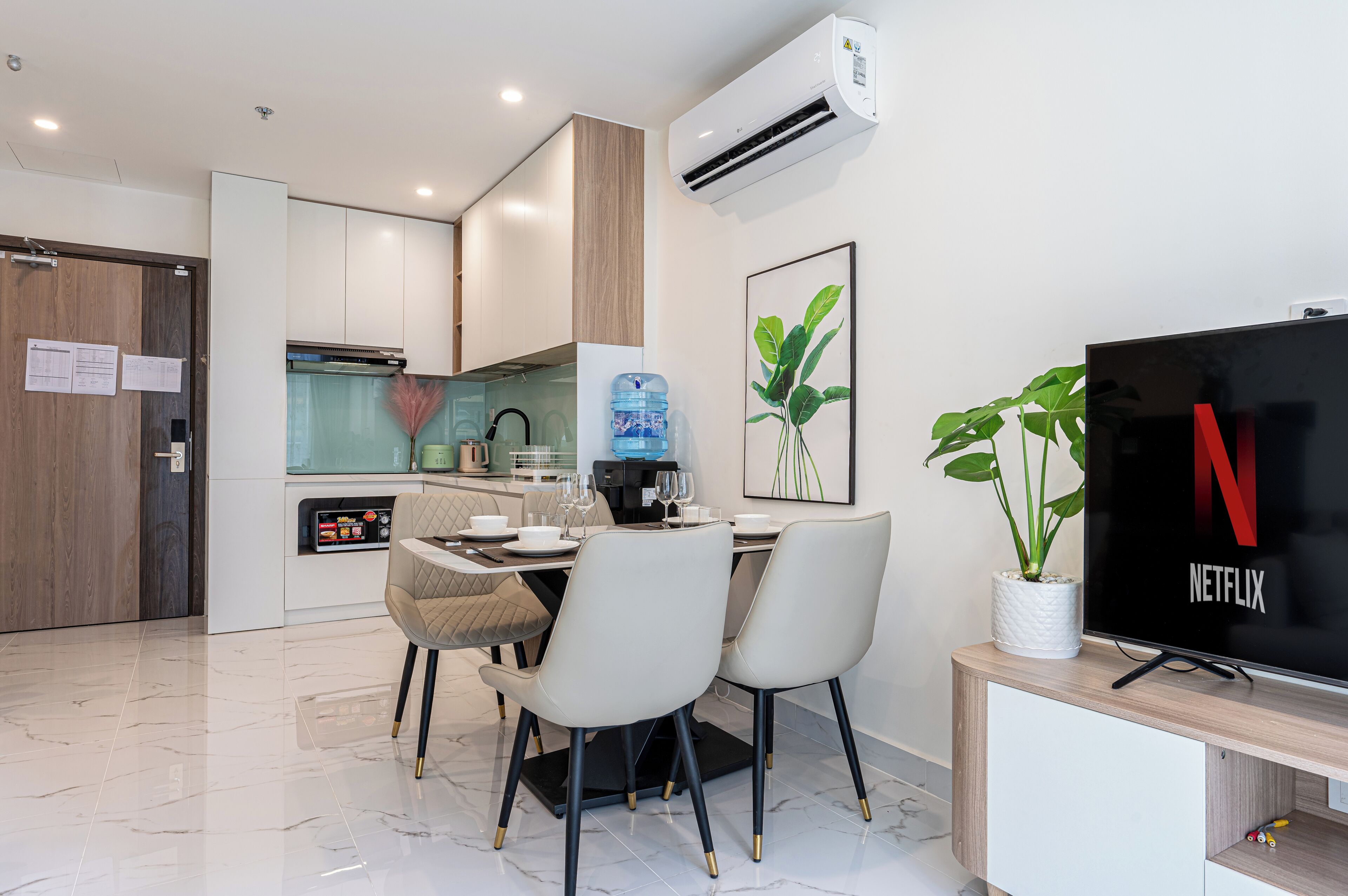 Una cocina moderna con comedor, un dispensador de agua grande y un televisor con Netflix sobre un mueble de madera.