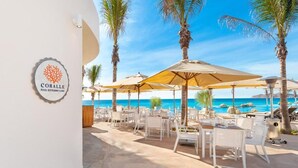Un restaurant situé au bord de la piscine, avec une terrasse, des palmiers et une vue sur l’océan.