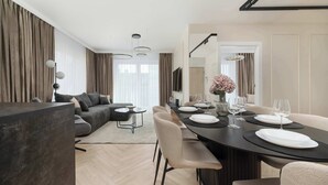 Un salon moderne avec un canapé foncé, une table à manger dressée pour quatre personnes et une grande fenêtre avec des rideaux.