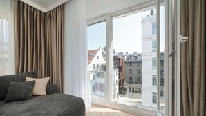 Un salon moderne avec un canapé gris, des coussins beige et une grande fenêtre avec des rideaux.