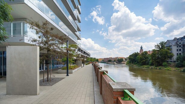 Une promenade au bord de la rivière, avec un bâtiment moderne, un pont et une tour qui se dresse au loin.