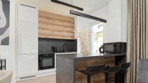 Une cuisine moderne avec des armoires blanches, un mur d’accent en bois, un four encastré, un four à micro-ondes et un coin bar avec des tabourets.