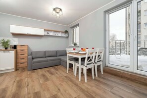 Ein stilvoller Wohnraum mit Essbereich, einem grauen Sofa, einer kleinen Küche und einem großen Fenster.