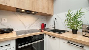 A modern kitchen with wooden cabinets, a built-in oven, a dishwasher, a sink, and a toaster. - Cozy Studio with Balcony | Parking in Garage (Łódź)
