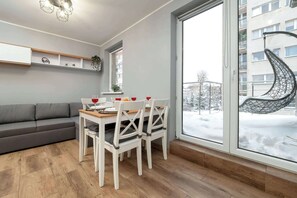 Een moderne woonkamer met een bank, eettafel, stoelen en een groot raam met uitzicht op een besneeuwde omgeving.