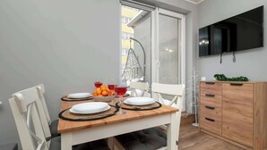 A dining area with a table set for two, a television mounted on the wall, and a wooden cabinet. - Cozy Studio with Balcony | Parking in Garage (Łódź)