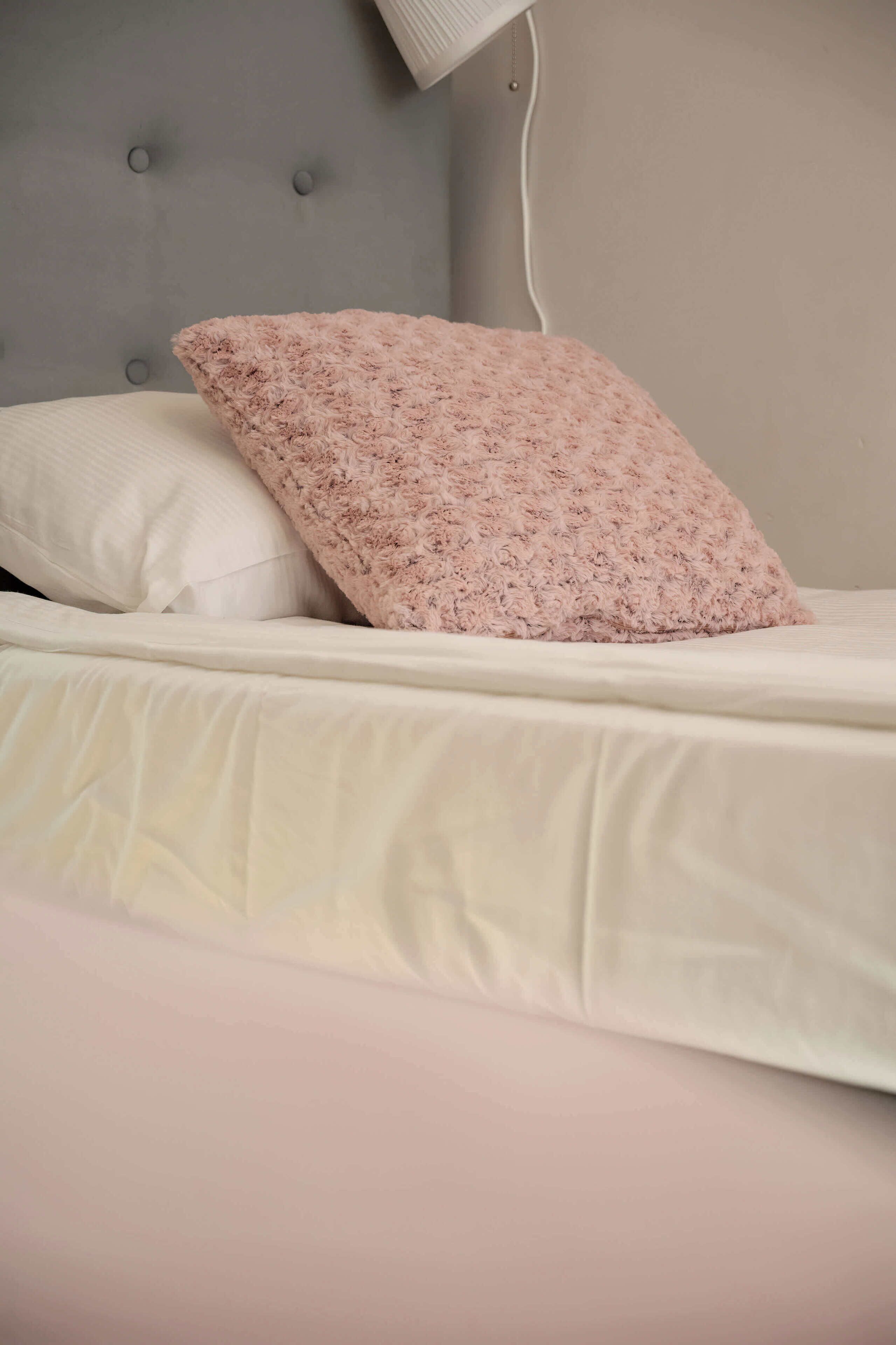 A bed with a tufted headboard, a white pillow, and a fluffy pink pillow.